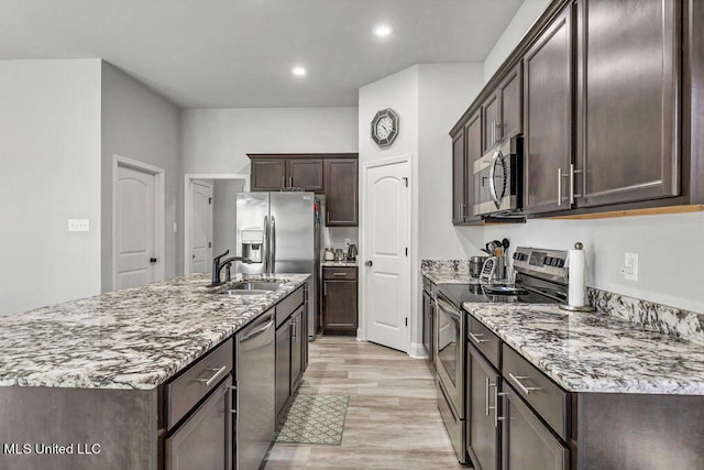 kitchen featuring dark brown cabinetry, sink, stainless steel appliances, light hardwood / wood-style flooring, and a kitchen island with sink