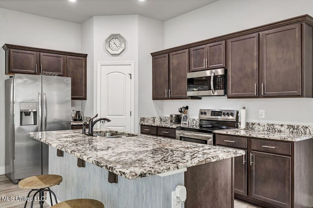 kitchen featuring light stone countertops, sink, stainless steel appliances, a kitchen island with sink, and a breakfast bar