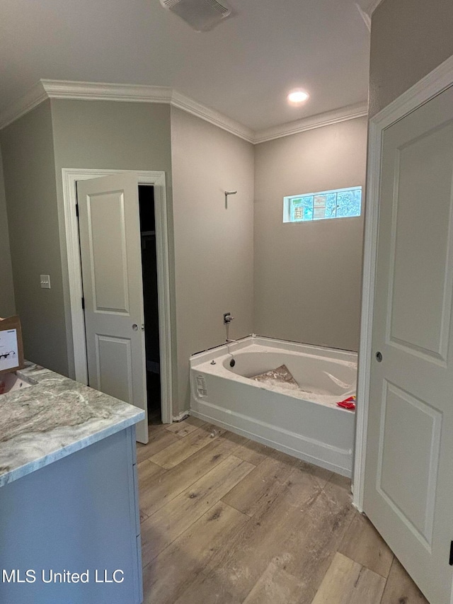 bathroom featuring vanity, wood-type flooring, ornamental molding, and a tub