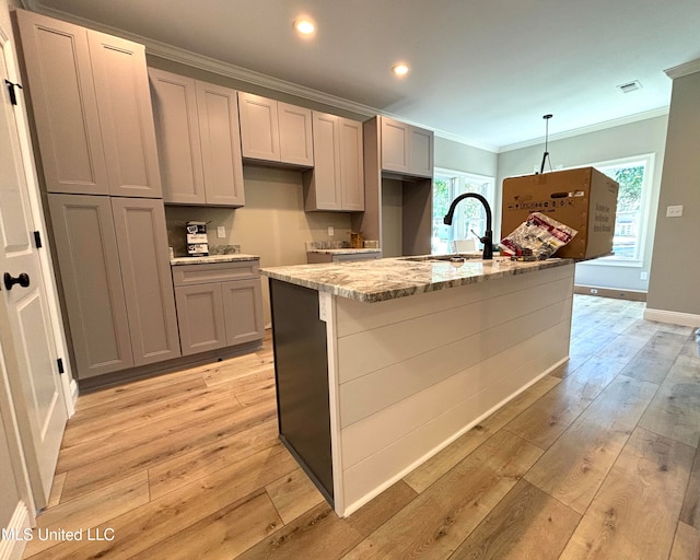 kitchen featuring sink, hanging light fixtures, gray cabinets, an island with sink, and light stone countertops