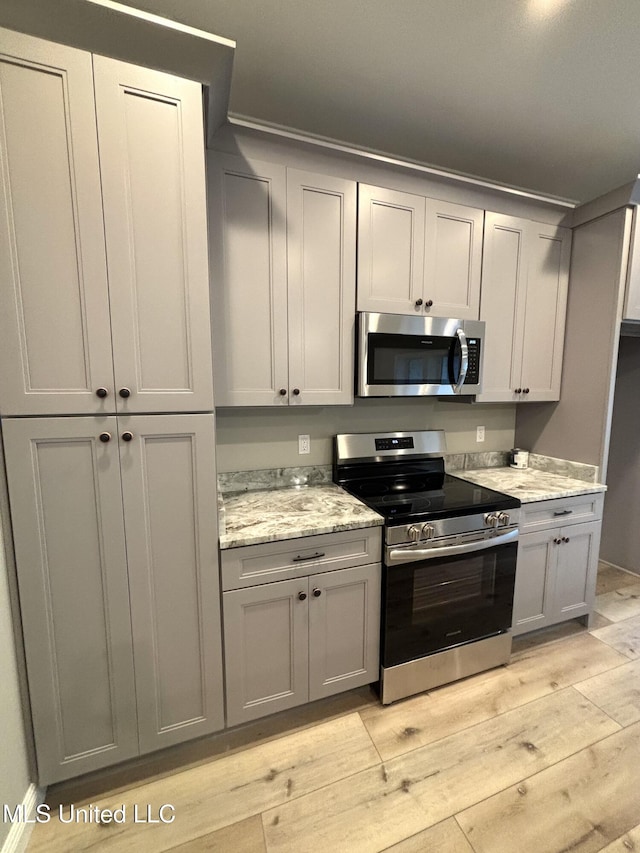 kitchen featuring light stone counters, stainless steel appliances, light hardwood / wood-style floors, and gray cabinetry