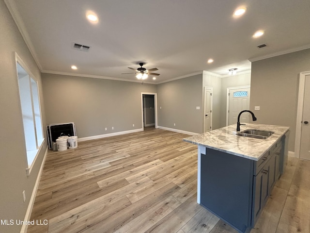 kitchen with sink, light stone counters, light hardwood / wood-style flooring, ceiling fan, and a kitchen island with sink