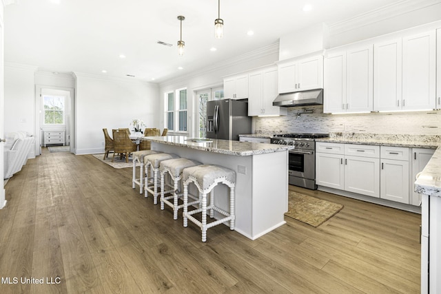 211 Chartres St, Bay Saint Louis, MS 39520 - kitchen with stainless steel appliances, under cabinet range hood, a center island, wood finished floors, and white cabinetry