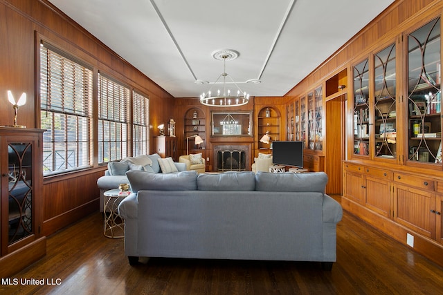 living room with wood walls, dark hardwood / wood-style floors, a notable chandelier, and built in shelves