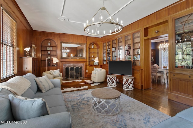 living room with dark hardwood / wood-style flooring, wooden walls, an inviting chandelier, and built in shelves