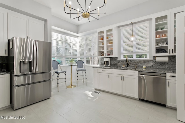 kitchen with appliances with stainless steel finishes, dark stone counters, pendant lighting, white cabinets, and a chandelier