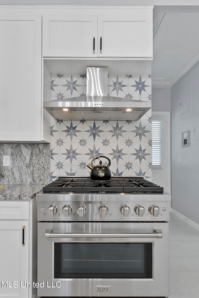 kitchen with wall chimney range hood, white cabinets, tasteful backsplash, and high end range