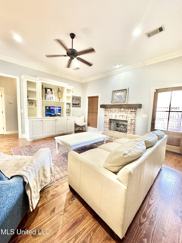 living room with ceiling fan, a fireplace, ornamental molding, and light wood-type flooring