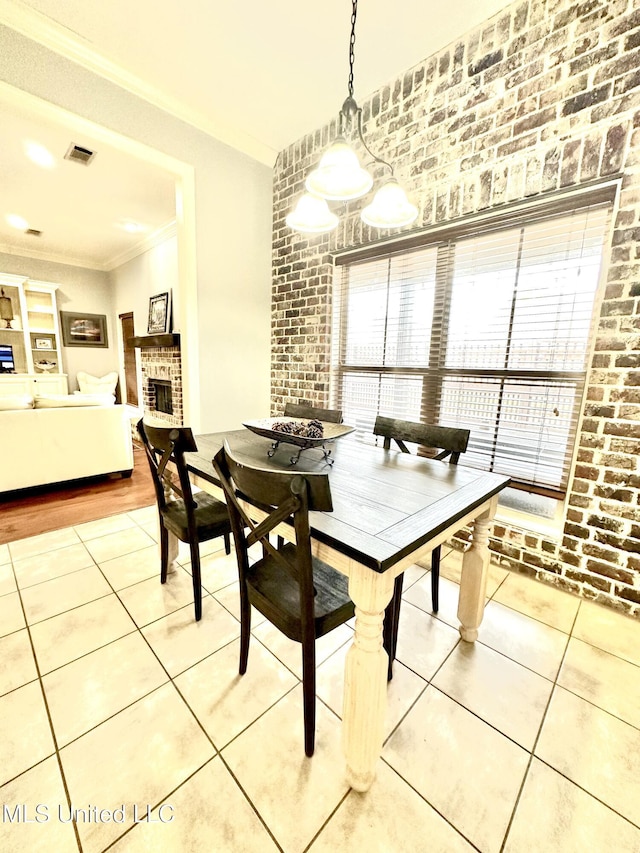 tiled dining area with ornamental molding, brick wall, and a brick fireplace