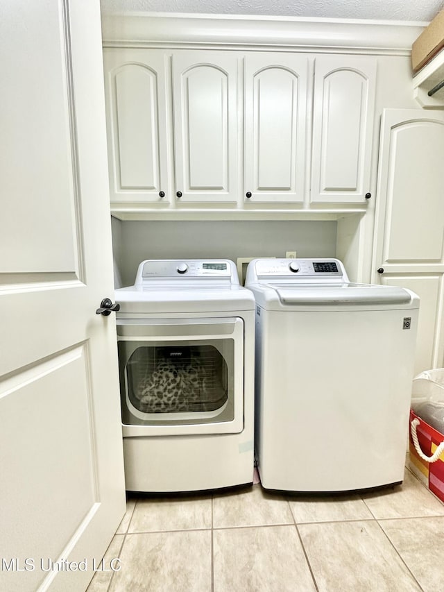 clothes washing area featuring separate washer and dryer, light tile patterned floors, cabinets, and a textured ceiling