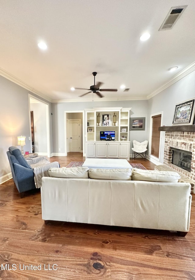 living room featuring ceiling fan, ornamental molding, dark wood-type flooring, and a brick fireplace