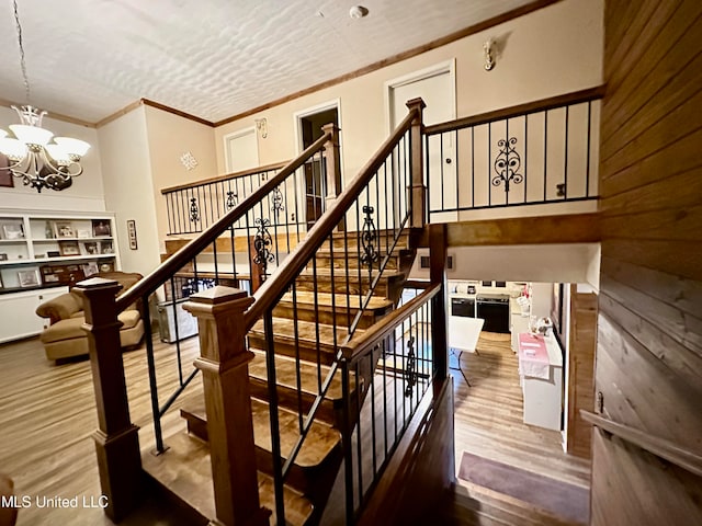 stairway with an inviting chandelier, hardwood / wood-style floors, wood walls, and crown molding