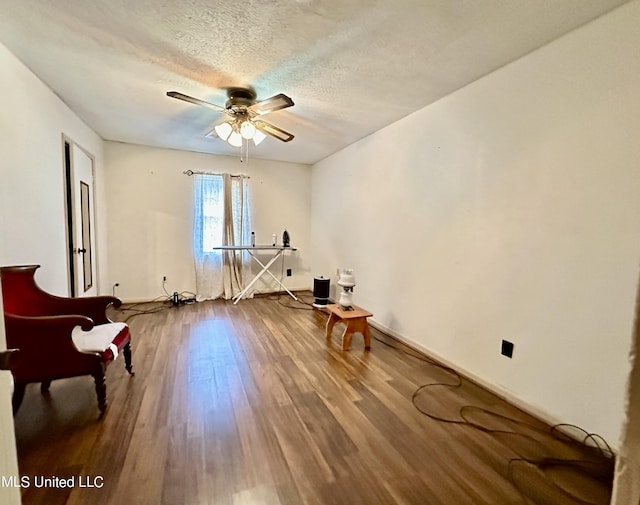 living area with a textured ceiling, wood-type flooring, and ceiling fan