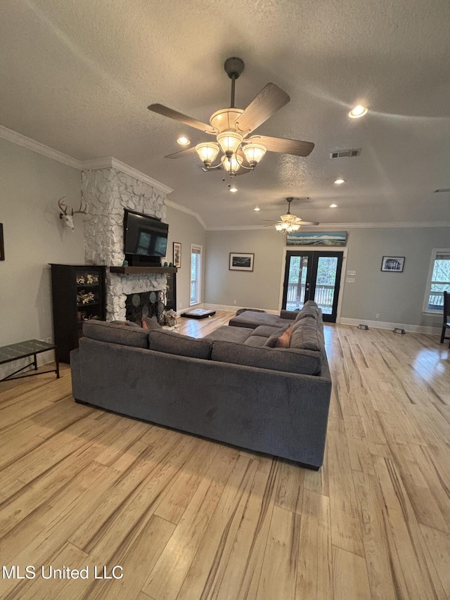 living room featuring ceiling fan, a stone fireplace, crown molding, a textured ceiling, and light wood-type flooring