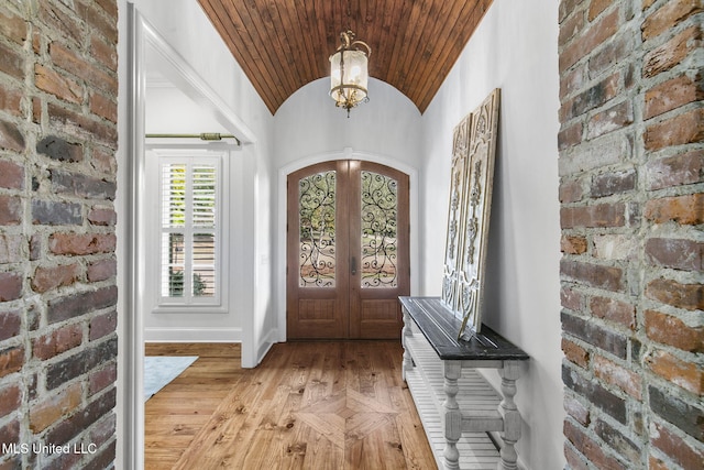 entryway featuring french doors, brick wall, a chandelier, and light wood-type flooring