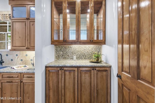 bar featuring backsplash, light stone countertops, and sink