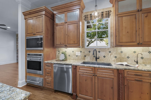 kitchen with crown molding, sink, decorative light fixtures, light wood-type flooring, and appliances with stainless steel finishes