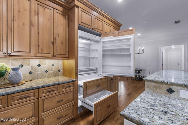 kitchen featuring dark hardwood / wood-style floors, hanging light fixtures, backsplash, crown molding, and light stone countertops