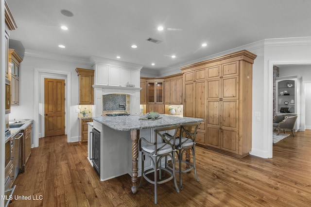 kitchen with light stone countertops, a center island, beverage cooler, crown molding, and dark hardwood / wood-style floors