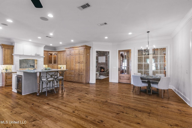 kitchen featuring a kitchen bar, a large fireplace, crown molding, a notable chandelier, and dark hardwood / wood-style floors