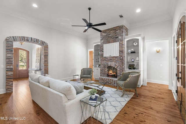 living room featuring crown molding, a brick fireplace, wood-type flooring, and ceiling fan