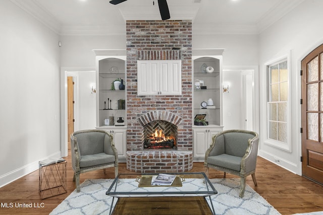 living room with hardwood / wood-style floors, ceiling fan, a fireplace, built in shelves, and crown molding