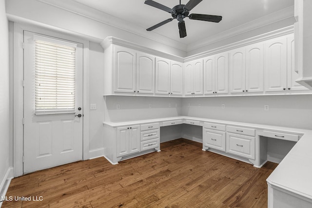 unfurnished office with ornamental molding, built in desk, dark wood-type flooring, and ceiling fan