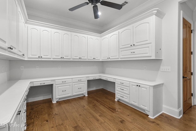 unfurnished office featuring ornamental molding, dark hardwood / wood-style floors, built in desk, and ceiling fan