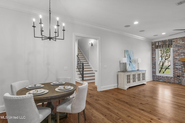 dining space with ceiling fan with notable chandelier, hardwood / wood-style flooring, ornamental molding, and brick wall