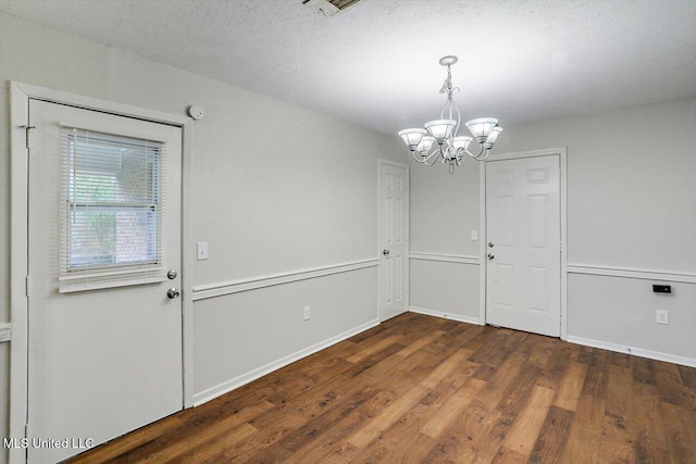 unfurnished dining area with an inviting chandelier, dark hardwood / wood-style floors, and a textured ceiling