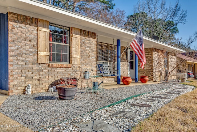 doorway to property featuring covered porch and brick siding