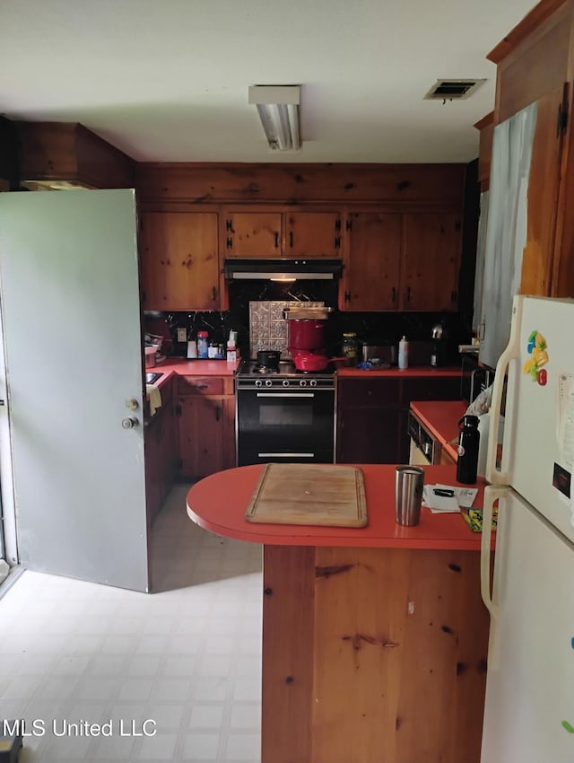 kitchen featuring freestanding refrigerator, electric range, decorative backsplash, under cabinet range hood, and tile patterned floors