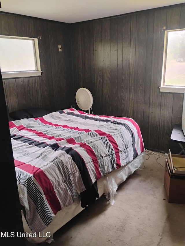 bedroom featuring wood walls, multiple windows, and unfinished concrete flooring