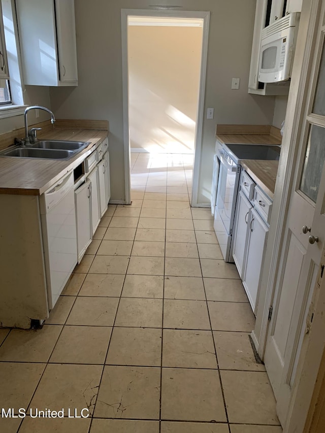 kitchen with white cabinetry, white appliances, light tile patterned floors, and a sink