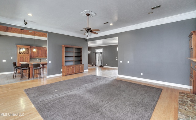 unfurnished living room featuring light hardwood / wood-style flooring, ornamental molding, a textured ceiling, and ceiling fan