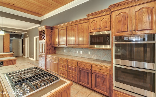 kitchen featuring decorative backsplash, tile counters, stainless steel appliances, ornamental molding, and light tile patterned floors