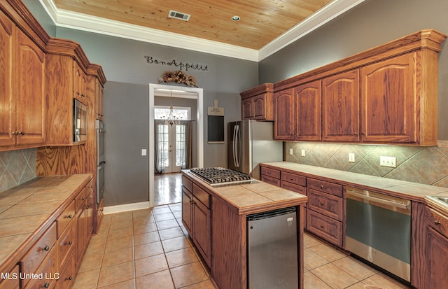 kitchen with appliances with stainless steel finishes, backsplash, wooden ceiling, tile counters, and ornamental molding