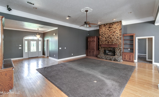 unfurnished living room featuring a stone fireplace, a textured ceiling, ceiling fan, hardwood / wood-style flooring, and ornamental molding