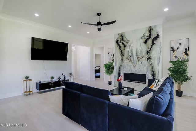 living room featuring ceiling fan, ornamental molding, light hardwood / wood-style flooring, and a fireplace