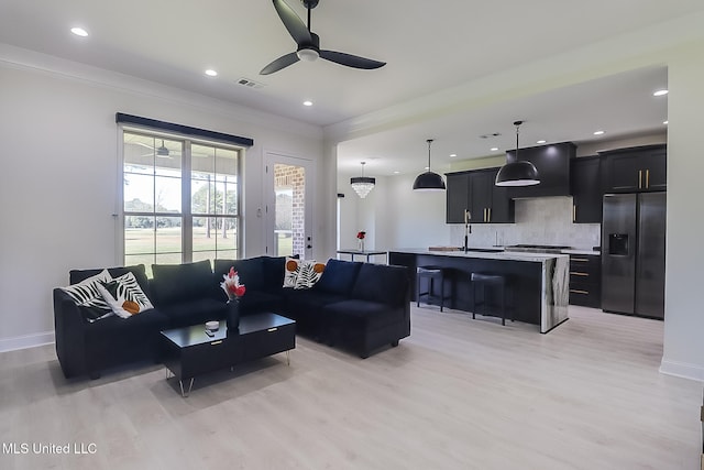 living room featuring sink, ceiling fan, ornamental molding, and light hardwood / wood-style flooring