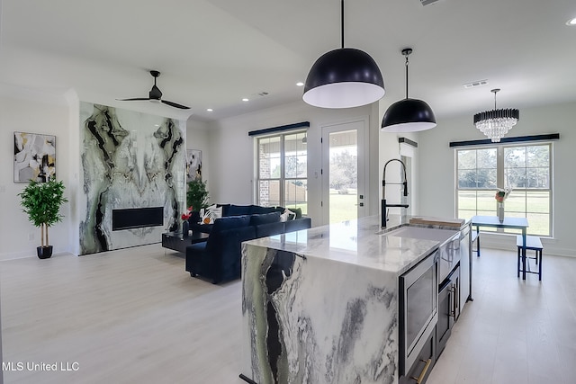 kitchen featuring light stone counters, a healthy amount of sunlight, decorative light fixtures, and a kitchen island with sink