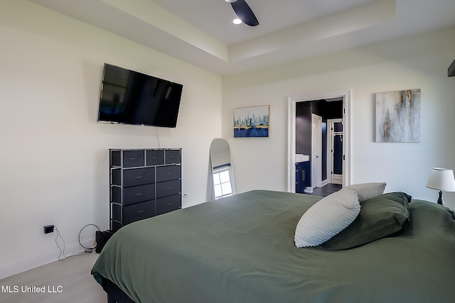 bedroom with connected bathroom, ceiling fan, a tray ceiling, and light hardwood / wood-style flooring