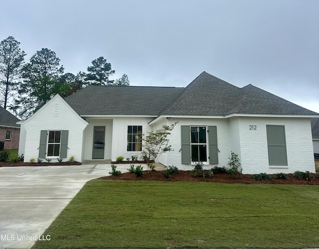 view of front of property with a shingled roof, a front yard, and brick siding