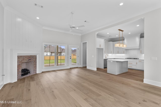 unfurnished living room featuring ornamental molding, light wood-style flooring, a ceiling fan, baseboards, and a brick fireplace