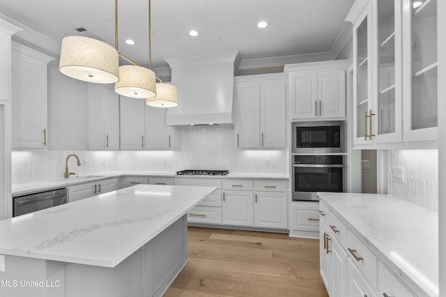 kitchen featuring stainless steel appliances, a sink, wall chimney range hood, crown molding, and white cabinetry