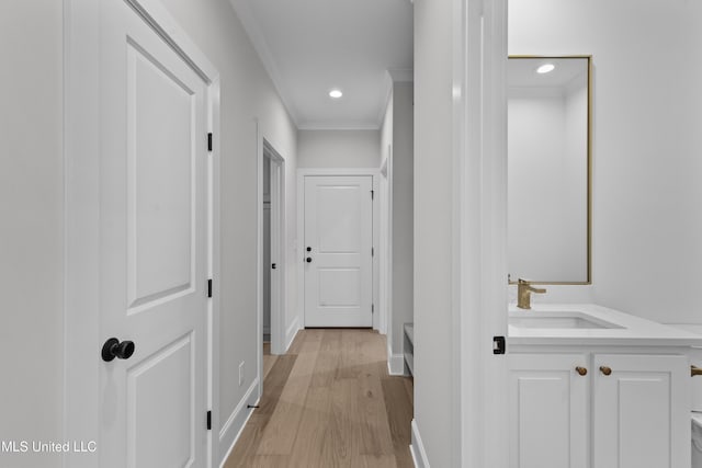 corridor with a sink, crown molding, light wood-style flooring, baseboards, and recessed lighting