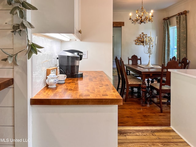 kitchen featuring butcher block counters, light hardwood / wood-style floors, pendant lighting, ornamental molding, and a chandelier