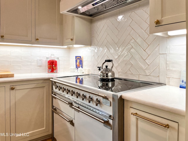 kitchen with custom range hood, decorative backsplash, cream cabinetry, and high end stove