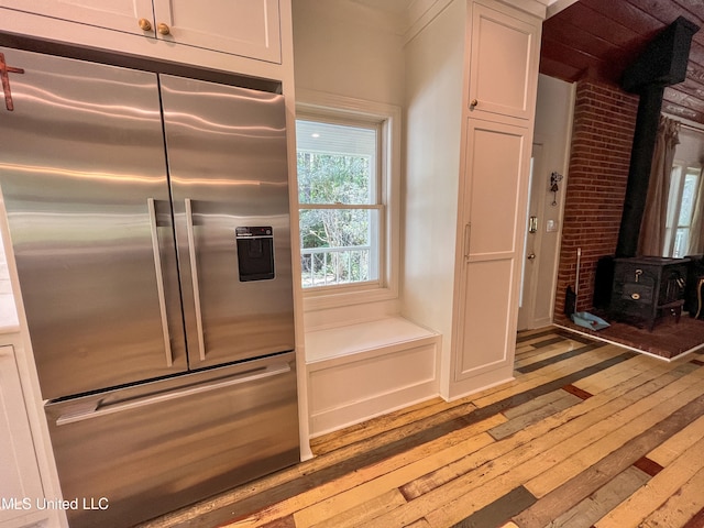 kitchen with stainless steel fridge with ice dispenser, white cabinetry, light wood-type flooring, and a wood stove