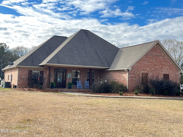 view of front facade featuring central AC unit, brick siding, roof with shingles, and a front yard